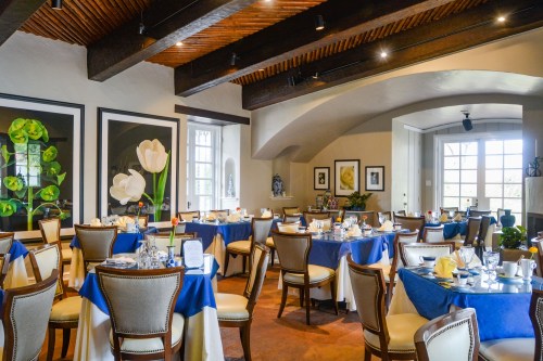 Elegant restaurant interior with blue and white table settings, large windows, and floral decor.