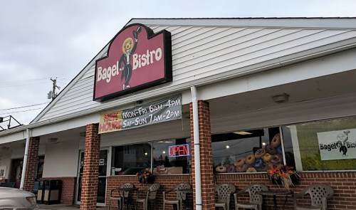 Exterior of Bagel Bistro with a sign, open hours displayed, and outdoor seating.