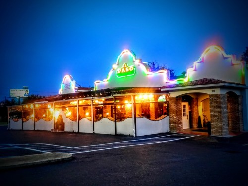 A brightly lit restaurant exterior at dusk, featuring colorful lights and a distinctive architectural design.