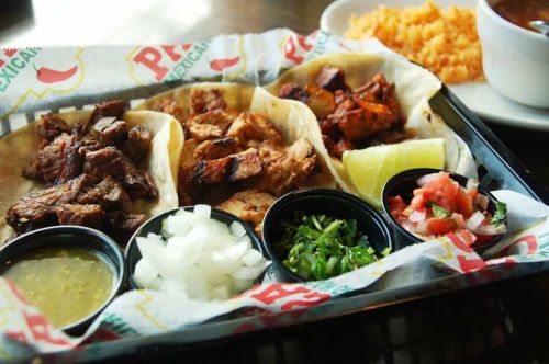 A platter of tacos with various meats, garnished with onions, cilantro, lime, salsa, and a side of rice.