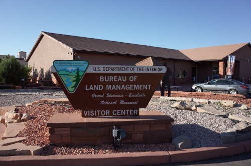 Sign for the Bureau of Land Management Visitor Center at Grand Staircase-Escalante National Monument, with a building in the background.