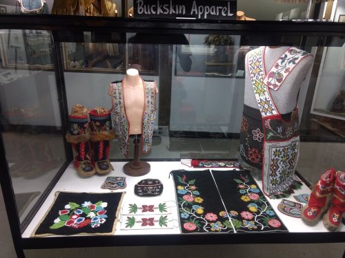Display case featuring colorful buckskin apparel, including vests, boots, and embroidered accessories.
