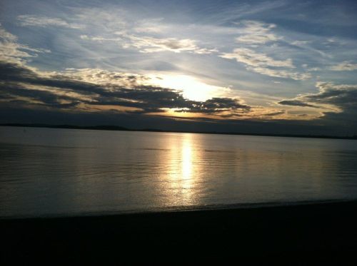 A serene sunset over calm waters, with clouds reflecting the golden light in a tranquil sky.