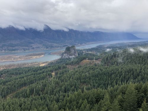 A scenic view of a river winding through mountains, with a prominent rock formation and dense evergreen forests.