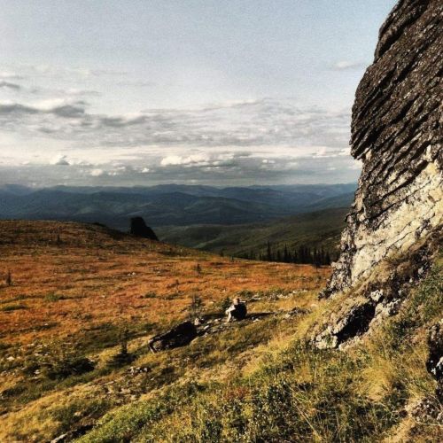 A rocky outcrop overlooks a vast, rolling landscape of hills and valleys under a cloudy sky.