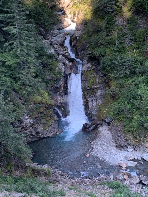 A scenic waterfall cascading down rocky cliffs into a clear pool, surrounded by lush greenery and trees.