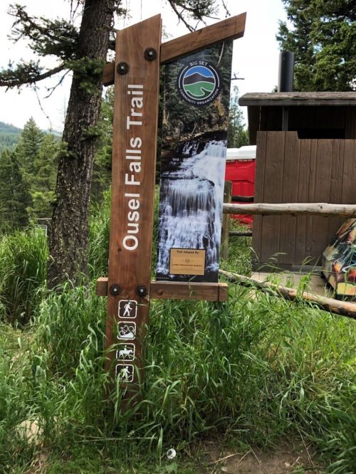 Signpost for Ouse Falls Trail, featuring a waterfall image and trail information, surrounded by greenery and trees.