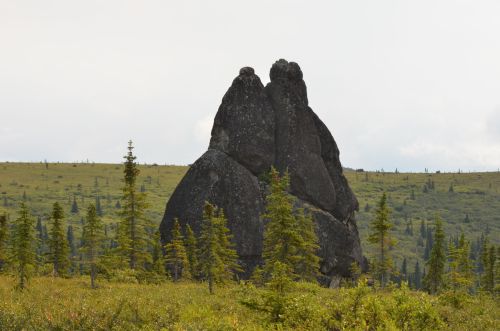 Two large, dark rock formations resembling a pair of figures stand amidst a green landscape with scattered trees.