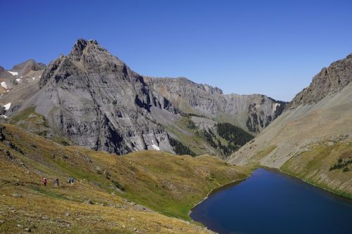 A scenic landscape featuring rugged mountains and a serene blue lake surrounded by grassy hills under a clear blue sky.