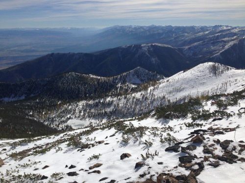 A panoramic view of snow-covered mountains and valleys under a clear sky, showcasing rugged terrain and distant peaks.