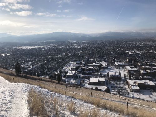 A snowy landscape overlooking a town with mountains in the background under a clear blue sky.