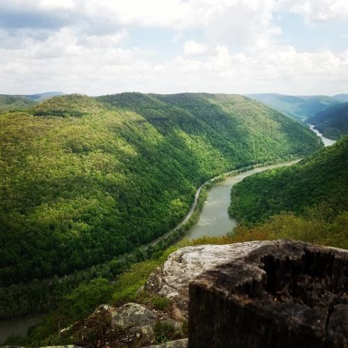 A scenic view of a winding river surrounded by lush green hills under a partly cloudy sky.