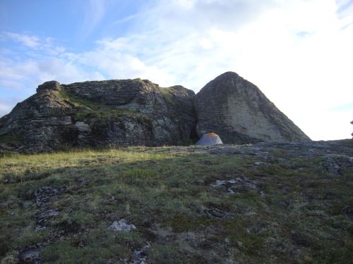 A tent set up on rocky terrain near two large, rugged rock formations under a cloudy sky.