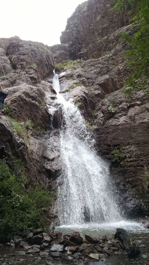 A cascading waterfall flows down rocky cliffs, surrounded by lush greenery and a small pool at the base.