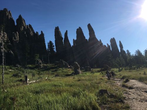 A scenic landscape featuring tall rock formations and a path, with sunlight shining over a grassy area.