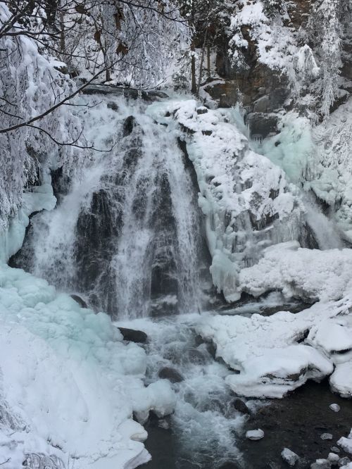 A frozen waterfall surrounded by snow-covered rocks and icy formations, creating a serene winter landscape.