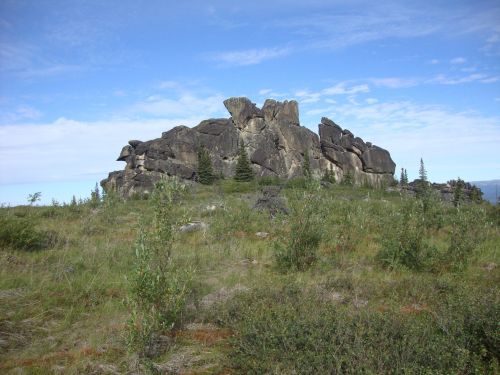 A rocky outcrop rises above a grassy landscape under a blue sky with scattered clouds.
