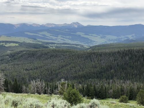 A panoramic view of rolling green hills and distant mountains under a cloudy sky.