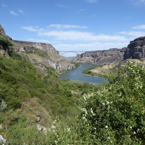 A scenic view of a river winding through a canyon, with a bridge spanning across the landscape under a blue sky.