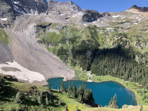 A serene mountain landscape featuring a turquoise lake surrounded by lush greenery and rocky slopes.