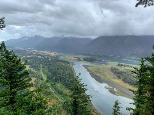 A scenic view of a winding river surrounded by lush greenery and mountains under a cloudy sky.
