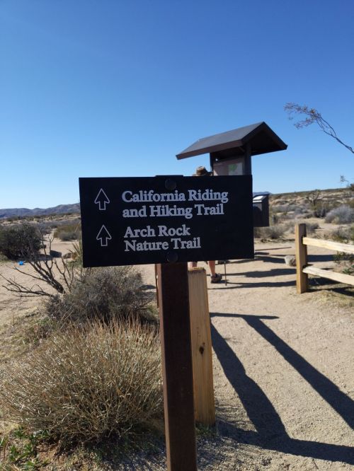 Signpost indicating directions for California Riding and Hiking Trail and Arch Rock Nature Trail in a desert landscape.