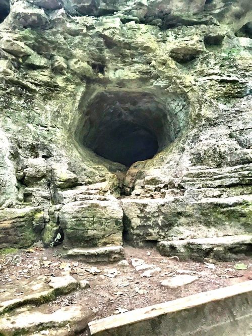 A rocky cave entrance surrounded by moss-covered stone, leading into darkness.