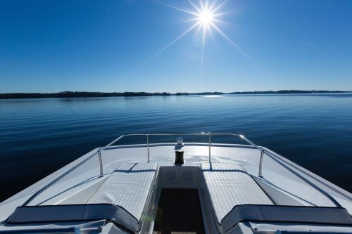 A serene view from the bow of a boat, with sun shining over calm waters and distant islands under a clear blue sky.