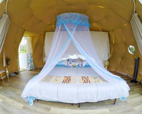 Cozy tent interior with a large bed draped in a blue canopy, surrounded by warm, earthy tones and natural light.