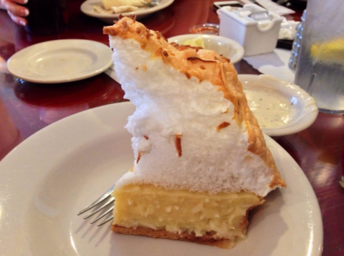 A slice of lemon meringue pie on a plate, featuring a golden filling and a fluffy white meringue topping.