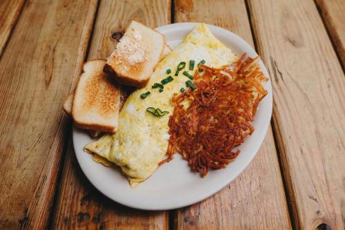 A plate with a fluffy omelette, crispy hash browns, and two slices of toasted bread on a wooden table.