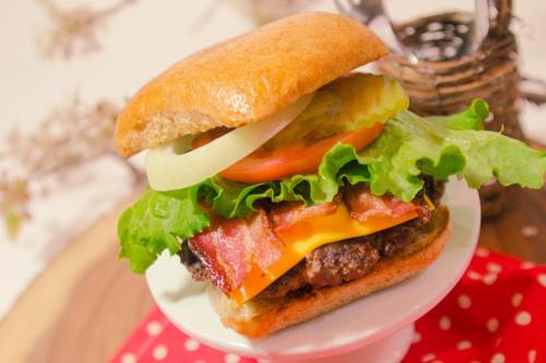 A delicious burger with lettuce, tomato, onion, pickles, bacon, and cheese on a whole grain bun, served on a white plate.