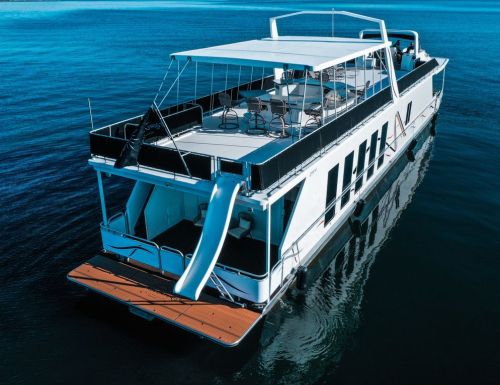 A spacious houseboat with a sun deck, moored on calm blue waters, featuring a slide and outdoor seating.