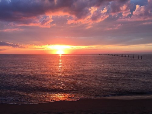 A vibrant sunset over calm waters, with colorful clouds and a silhouette of a pier in the distance.