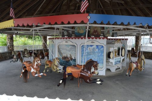 A vintage carousel with painted horses, colorful canopies, and murals, set in a shaded pavilion.