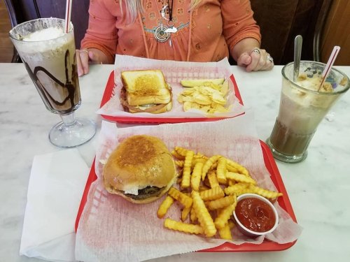 A table with two trays of food: a burger with fries and ketchup, a sandwich with chips, and two milkshakes.