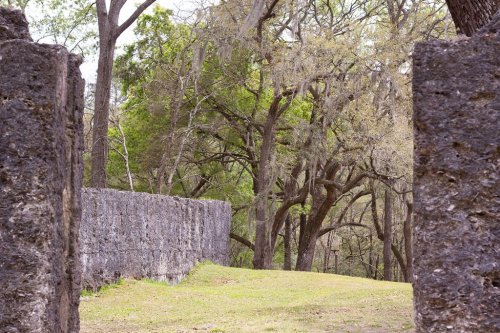 Stone walls frame a view of lush green trees and grass in a serene outdoor setting.