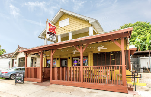 A yellow two-story building with a porch, featuring a sign for a restaurant and outdoor seating.