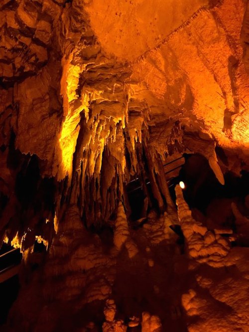 Stalactites and stalagmites illuminated in warm orange light inside a cave.