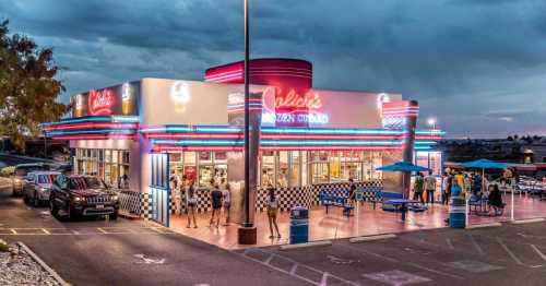 A retro-style ice cream shop with neon lights, outdoor seating, and customers enjoying the evening atmosphere.