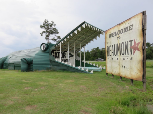 A large alligator-shaped building with a sign welcoming visitors to Beaumont, Texas, set in a grassy area.