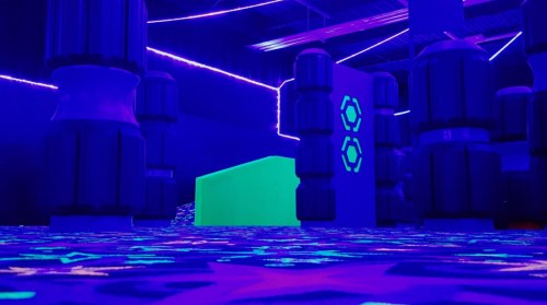 A vibrant, neon-lit indoor space with glowing obstacles and a bright green structure, creating a futuristic atmosphere.