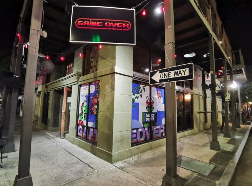 A corner building with a neon "GAME OVER" sign and colorful video game-themed window art, illuminated at night.