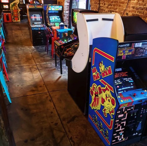 A retro arcade with various classic game machines and colorful cabinets lining the walls.
