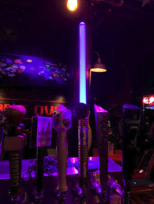A dimly lit bar with colorful beer taps, featuring a glowing blue light in the center.
