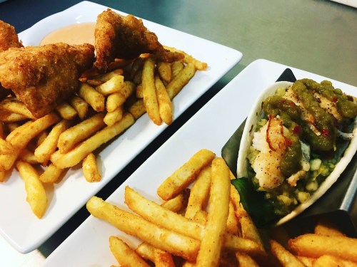 Two plates of food featuring crispy fried fish, golden French fries, and a side of seafood with green sauce.