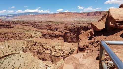 A panoramic view of rugged red rock formations and canyons under a blue sky with scattered clouds.