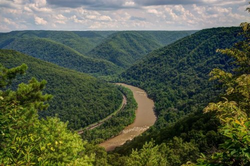 A winding river flows through lush green mountains under a partly cloudy sky.