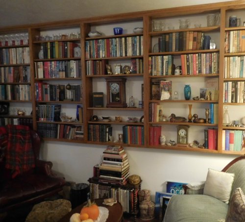 A cozy room with a wooden bookshelf filled with books, decorative items, and a comfortable chair.