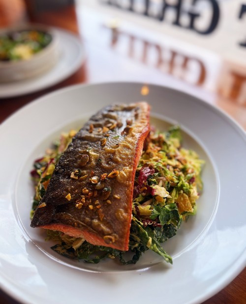 A plated dish featuring crispy salmon on a bed of mixed greens and chopped vegetables, garnished with nuts.